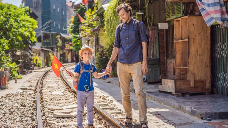 A kid holding the Vietnam flag on a railway track in Hanoi with his dad.