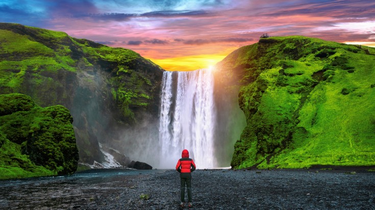 A man facing towards Skógafoss waterfall and admiring it.