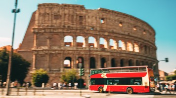 A red double-decker bus passing the Colosseum, headed to Naples from Rome.