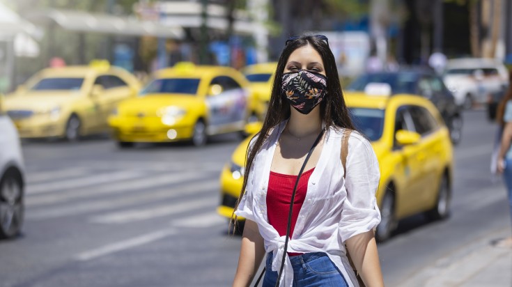 Tourist woman wearing a cloth face mask walks on the busy streets of Athe