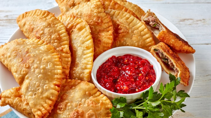 Deep fried buffalo chicken Empanadas with red hot sauce on a plate.