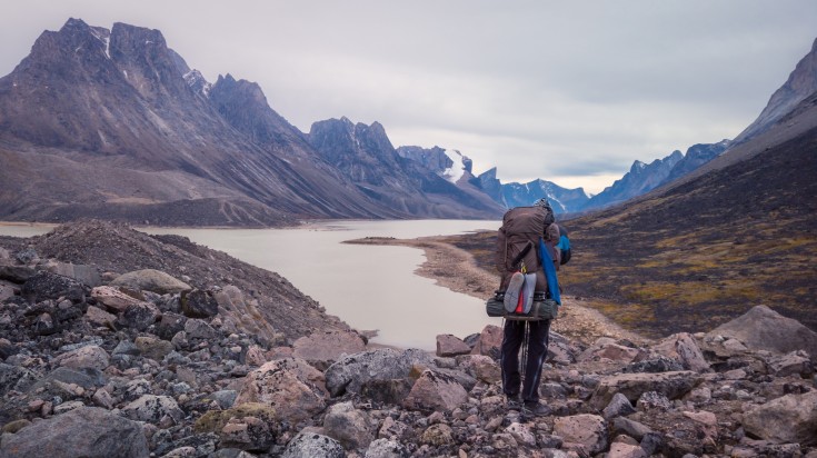 Hiker walking by Summit lake in remote arctic valley on a cloudy day.