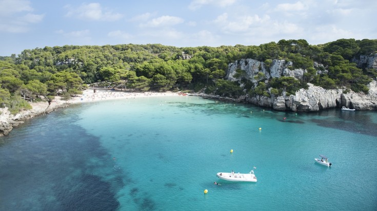 Two boats on the water on Cala Macarella beach surrounded by trees.