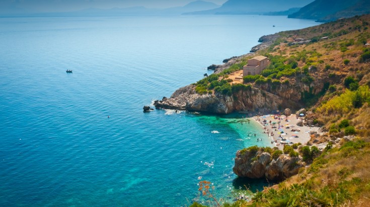 An arial perspective of Zingaro Nature Reserve with blue water, hills, and people enjoying on the beach. 