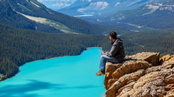 A man sitting at the edge of a cliff looking at Peyto Lake and the mountains in Icefields Parkway. 