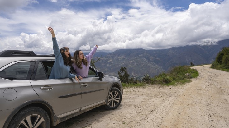 Two women protruding from car window with arms raised on their way from Lim