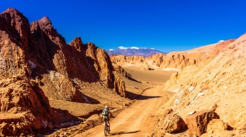 Atacama Desert's landscape has lots of activities for both the adventurous traveler and those interested in archeology. A traveler cycles on a stretch of road between two rocky formations