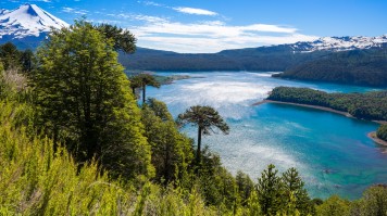 Blue lake surrounded by green hills and snow-capped mountains