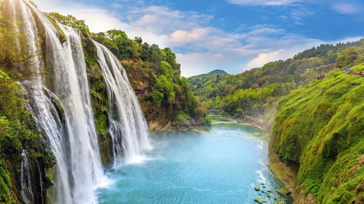 A waterfall in Guizhou surrounded by greenery on a bright day.