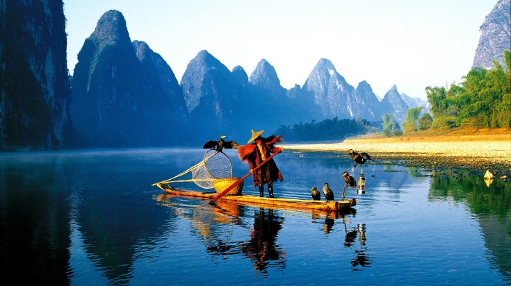 Fisherman on the Li River, surrounded by mountains, in China in June.