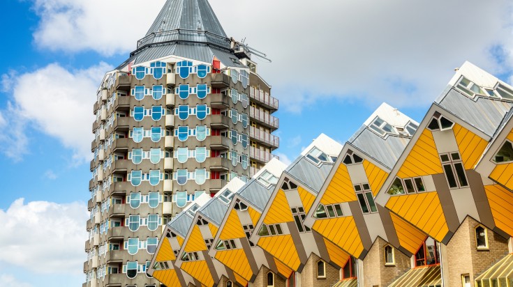 Yellow colored cubic houses in front of a modern building in the center of