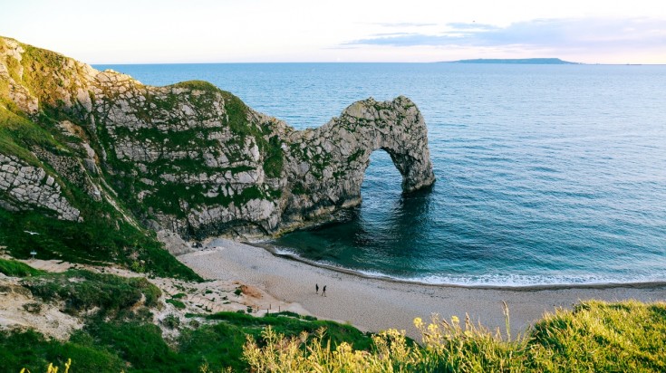 Two people walking on the Durdle door beach overlooking the sea