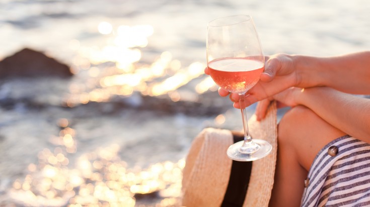 Girl is sitting on sea beach with wineglass of wine at sunset