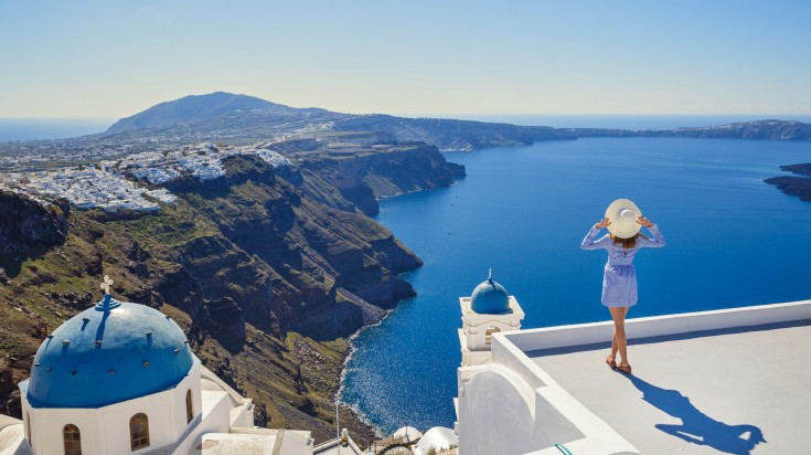 Young woman stands on a hill and looks at the marine landscape of Santorini