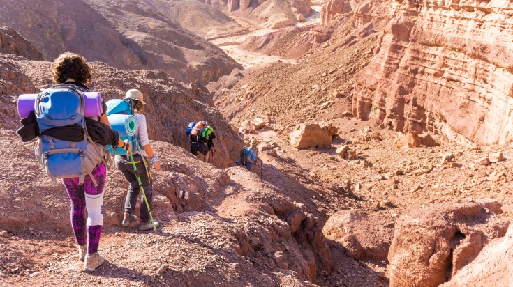 Group backpackers people hiking mountains in Negev desert in Israel.