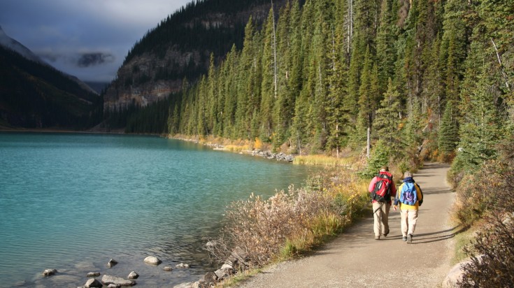 An elderly couple walking beside Lake Louise in Canada in July.