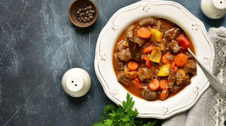 Meat stew with vegetables with cutlery and dishes on the table.