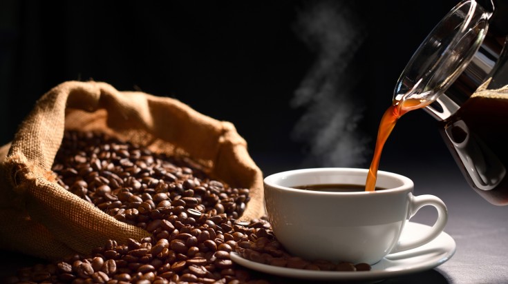 Coffee being poured in a cup with beans at the side.