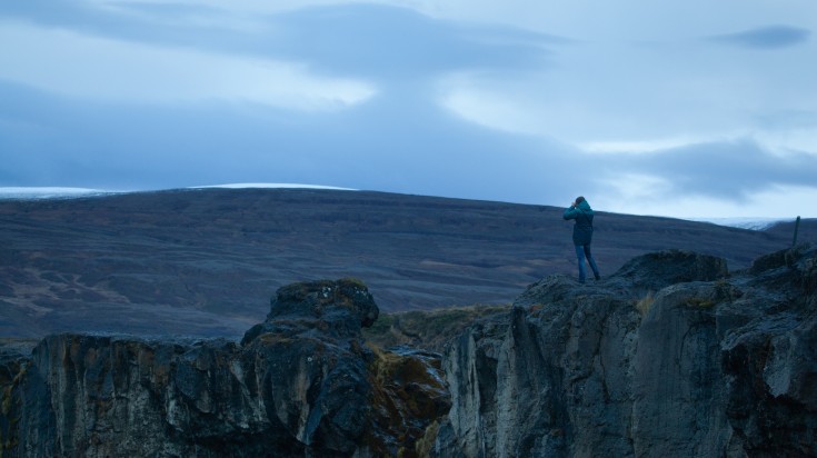 Sole traveler taking picture at dusk at Godafoss waterfall, Iceland