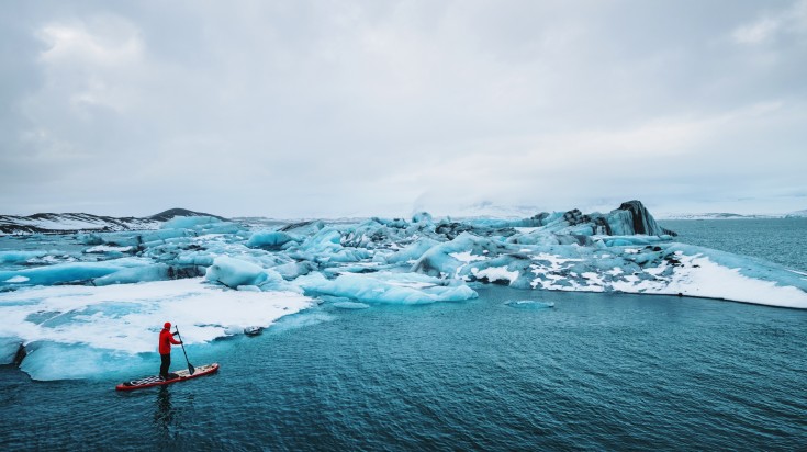 Beautiful view of icebergs glacier lagoon with a guy paddle boarding.