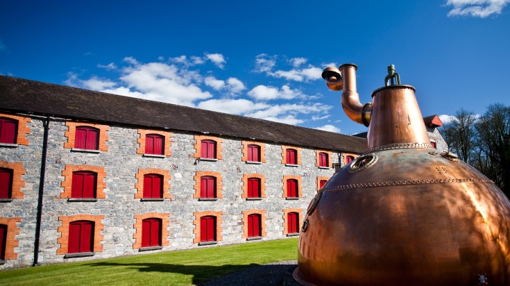 Old big copper whiskey distillery on stone foundation in Ireland.