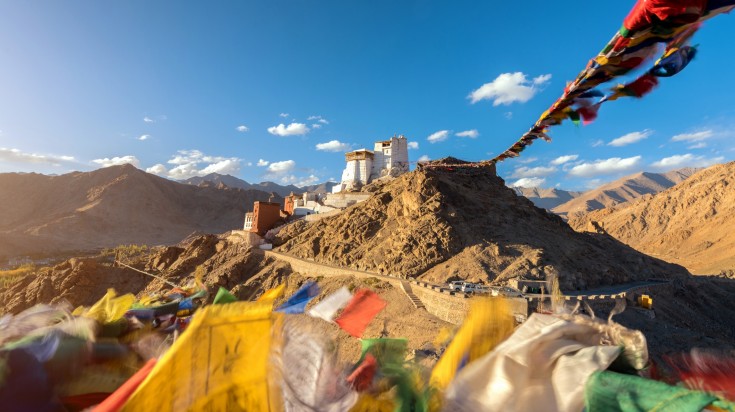 Prayer flags moving with the wind with Buddhist Monastery in the distance in Leh-Ladakh, India