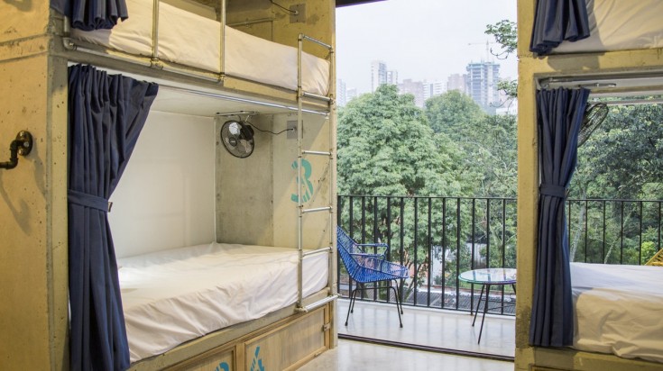 Bunk beds in a room with two chairs in the balcony overlooking the city at Los Patios Hostal Medellin. 