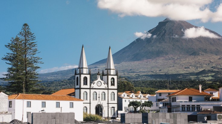 A white-walled church amidst white-washed buildings with tiled roofs against a naked hill