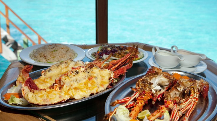 Plates of lobster on a table with ocean view in the Maldives.