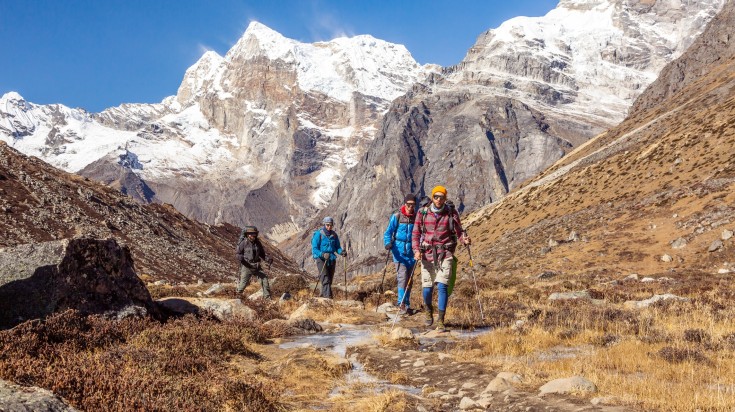 A group of hikers walk along the mountain trail in a line.