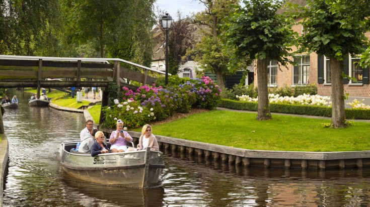 Tourists on a boat in a canal surrounded by greenery in Giethoorn.