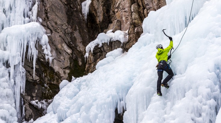 A man wearing climbing gears and harness and climbing icy, rocky mountain