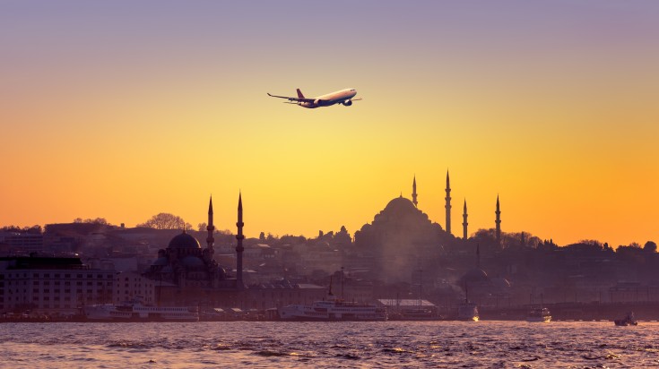 See a plane fly over Istanbul in Turkey during sunset.