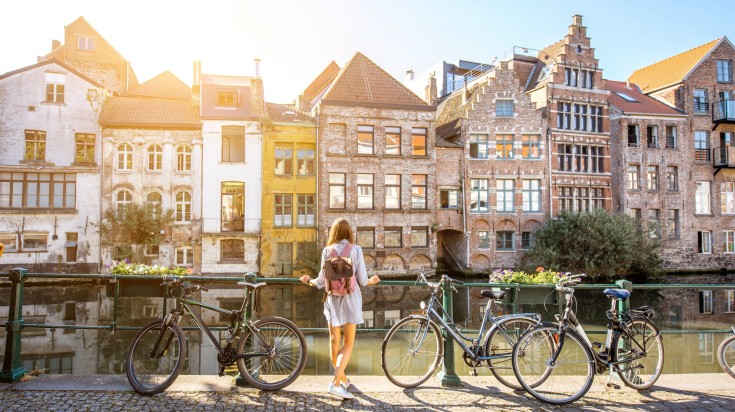A woman standing near bicycles in front of old buildings in Ghent.