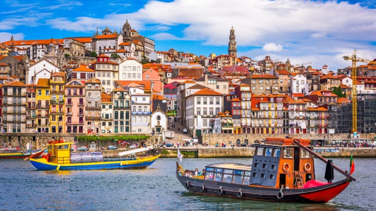 A view of Porto with boats on the river and compact houses in the background on a clear day in Portugal. 