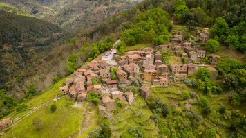 A cluster of old stone houses on top of a lush hill surrounded by forests
