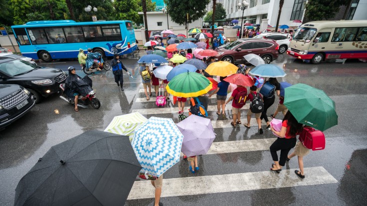 Street with crowded people using umbrella while touring Vietnam in July.