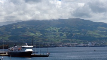 A ferry ship anchored at a port with lush green hilly landscape behind
