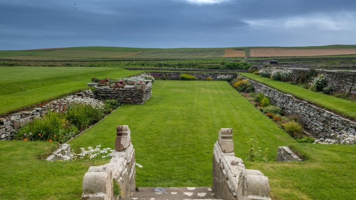 An overcast day at Skara Brae with green fields.