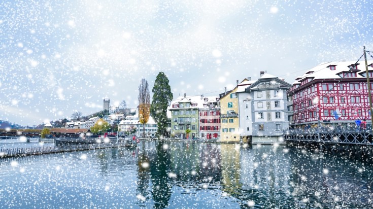 Snow falling over the city of Lucerne over a lake.