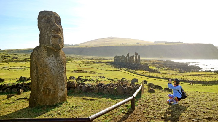 A woman taking picture of Solitary Moai on Easter Island, Chile.