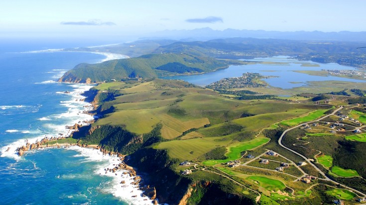 A bird's eye view of Garden Route Road Trip in South Africa with green hills and water all around. 