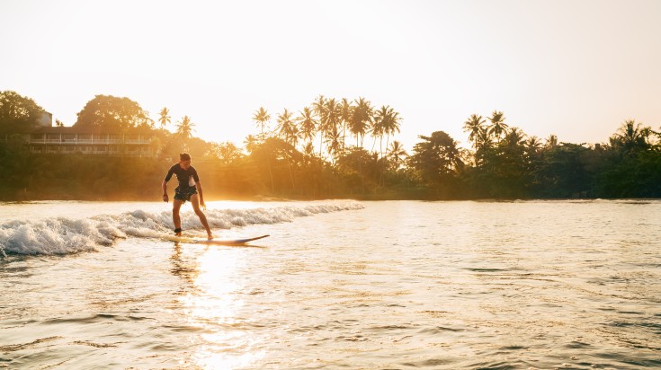 A boy riding long surfboard during dusk in Arugam Bay.