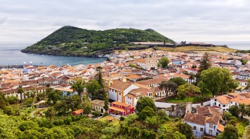 A white-washed town on an island with a lush mountain in the background