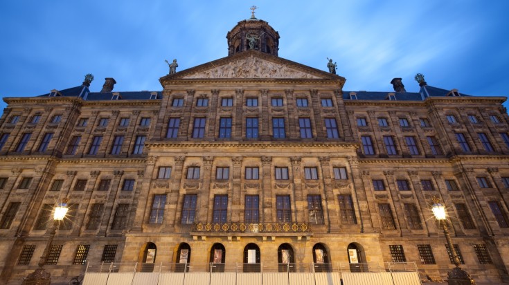 The Dutch Royal Palace illuminated against blue sky in the Netherlands.