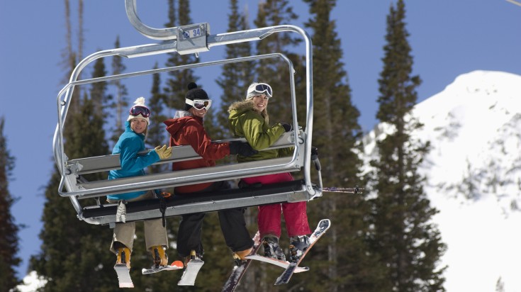 Three skiers enjoying a chairlift ride to their ski resort.