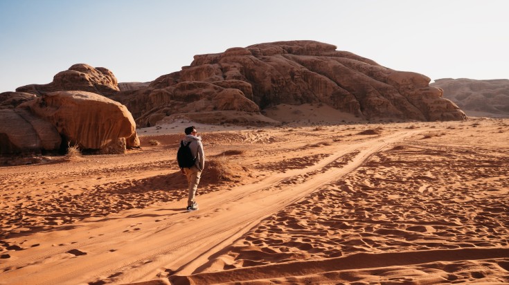 A hiker man walking in the Wadi Rum desert on a clear day.