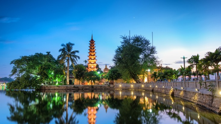 Well-lit Tran Quoc Pagoda and West Lake in Hanoi during evening time.