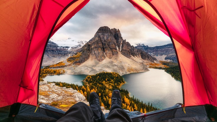 A man relaxing in his tent in autumn with a view of Mount Assiniboine in Canada in October. 