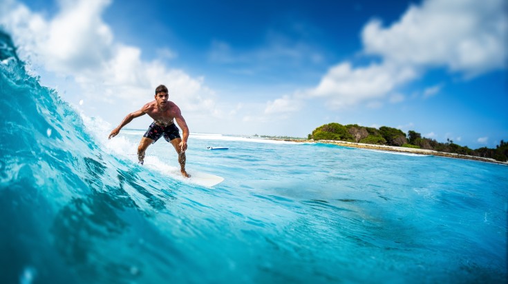 Young athletic surfer rides the ocean wave on Sultans surf spot in the Maldives.